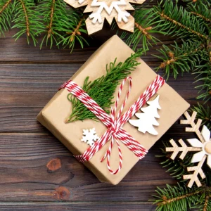 Christmas gift wrapped in kraft paper with red and white twine, pine sprigs, and wooden snowflake ornaments