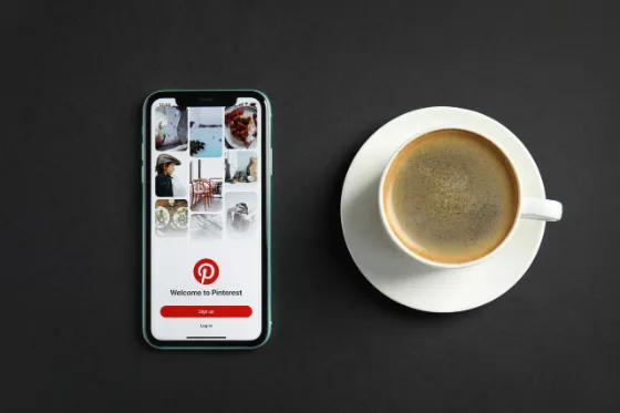 Person holding a smartphone with Pinterest open next to a laptop